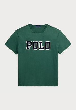 T-shirt verde de algodão com gola redonda e mangas curtas. Logótipo "POLO" em letras grandes na cor azul-marinho no peito. Textura suave.