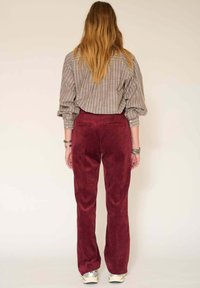 Pantalon en velours côtelé bordeaux avec une coupe droite, associé à une chemise rayée grise, affichant des détails de bouton et des manches retroussées.