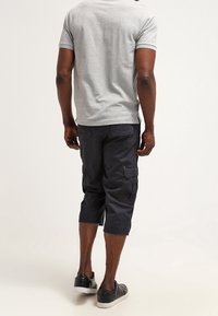T-shirt gris à manches courtes assorti à un short cargo sombre, avec deux poches latérales, une coupe jusqu'au genou, porté avec des baskets noires.