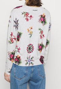 Gray sweatshirt featuring a floral pattern in vibrant colors. Long sleeves, round neck, and slightly loose fit. Printed logo on the back.