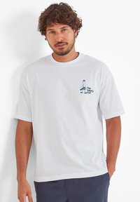 White cotton t-shirt with short sleeves and a round neckline. Features a printed graphic in blue on the left chest area.
