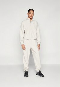 Pullover in pile beige chiaro con mezza cerniera e polsini elastici, abbinato a joggers in pile coordinati con vita elastica. Scarpe da ginnastica nere.