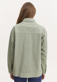 Ljusgrön jacka i texturerat tyg, med krage, knappade manschetter och en avslappnad passform med rak fåll.