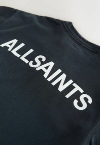 Čierna mikina s obyčajným okrúhlym výstrihom s nápisom "ALLSAINTS" vytlačeným veľkými bielymi písmenami na zadnej strane.