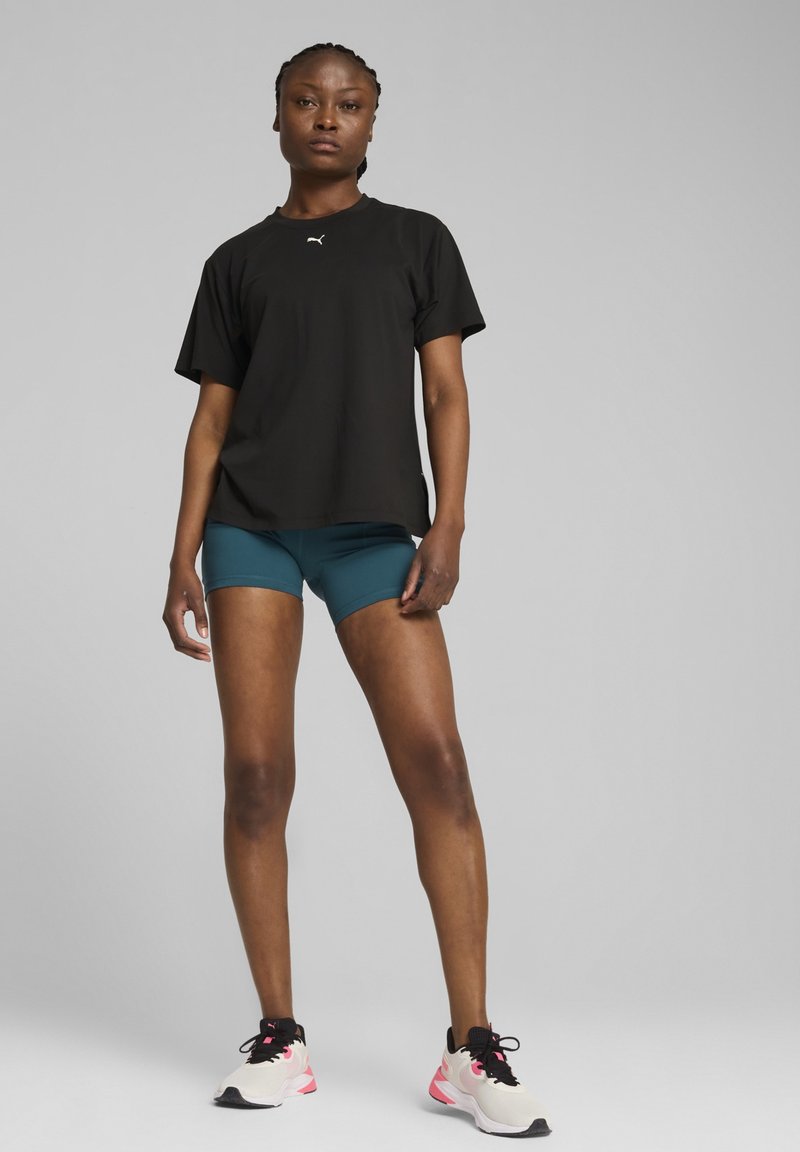 Zwart sport t-shirt met korte mouwen, gecombineerd met teal shorts. Schoenen zijn licht met roze accenten. Glad materiaal, comfortabele pasvorm.