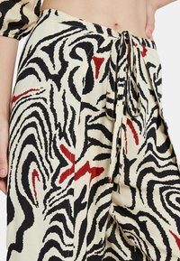 Pantalones sueltos con estampado en crema con rayas de cebra negras y acentos rojos. Cuentan con un lazo en la cintura y un tejido suave y texturizado.