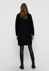 Black, oversized sweater dress with long sleeves, smooth texture, and minimalist design, paired with black leggings and knee-high boots.