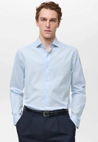 Camicia a righe blu chiaro con colletto a punta, maniche lunghe e pattina dei bottoni, abbinata a pantaloni scuri e una cintura nera.