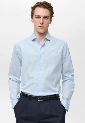 Helle blaue gestreifte Hemdbluse mit spitzem Kragen, langen Ärmeln und Knopfleiste, kombiniert mit dunklen Hosen und einem schwarzen Gürtel.