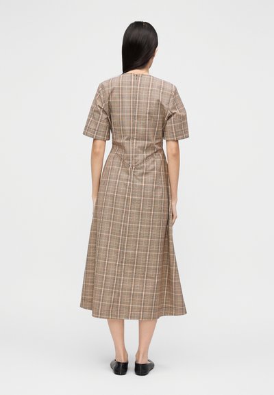 Καφέ καρό φόρεμα με κοντά μανίκια, μήκος μέχρι τη μέση της γάμπας, εφαρμοστό μπούστο και φούστα που φαρδαίνει. Διαθέτει κατακόρυφες ραφές και διακριτικές χρωματικές αποχρώσεις.