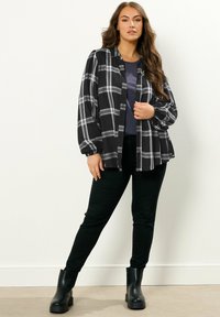 Camicia a scacchi bianca e nera con maniche lunghe, abbinata a un top scuro e pantaloni skinny neri. Indossata con stivali neri robusti.
