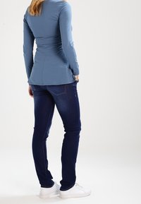 Camiseta de manga larga de color azul claro con un diseño ajustado, combinada con jeans skinny de color azul oscuro y zapatillas blancas. Tela suave, con un detalle mínimo.