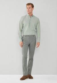 Lichtgroen button-down shirt met een subtiele textuur, gecombineerd met grijze slim-fit broek en bruine suède schoenen. Eenvoudig ontwerp, moderne snit.