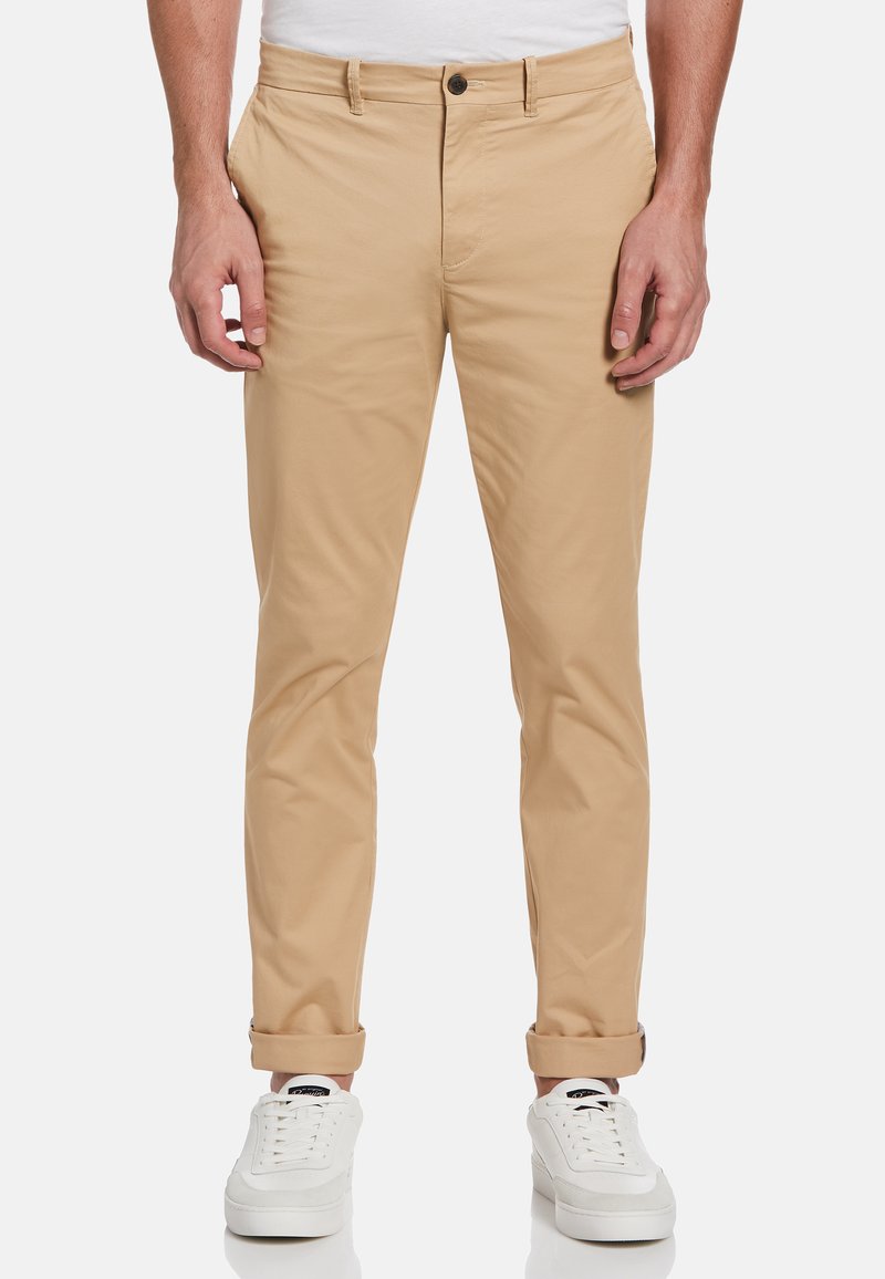 Beige katoenen chinos met een slanke pasvorm, voorzien van een knoopsluiting, zijzakken en opgerolde mouwen. Draagt met witte sneakers.