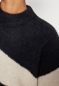 Pulover din tricot bleumarin și crem, cu o textură moale și pufoasă, având guler rotund și dungi diagonale în culori contrastante.