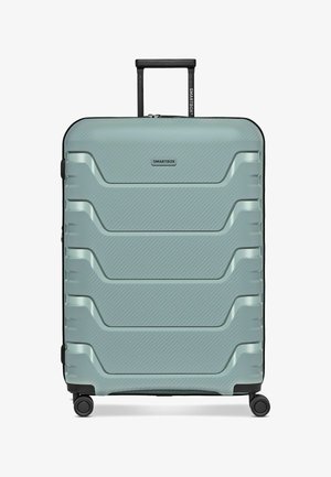 Valigia rigida verde chiaro con quattro ruote, manico telescopico nero e scanalature orizzontali testurizzate sul pannello frontale.