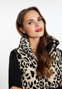 Plyšová vesta s leopardím potiskem, prošívaný design, černé akcenty a vysoký límec. Pod tím černý top s dlouhým rukávem, hladká textura.
