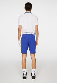 Hvid polo skjorte med blå krave, blå shorts og hvide sokker synlige. Inkluderer et hvidt bælte og lyse sneakers, med en golfhandske på venstre hånd.