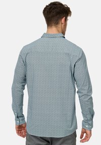 Langærmet skjorte i lyseblå med et lille, gentagende hvidt mønster. Har spids krave og knapmanchetter. Glat stofstruktur.