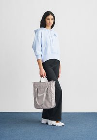 Φωτεινό γαλάζιο φαρδύ φούτερ με τσέπη καγκουρό, συνδυασμένο με μαύρα κολάν. Γκρι τσάντα ώμου με λευκό λογότυπο. Λευκά αθλητικά παπούτσια.