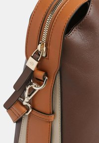 Bolso de cuero marrón con acentos en color beige, con un zipper de tono dorado y un clip metálico. Textura suave con bandas de color contrastantes.