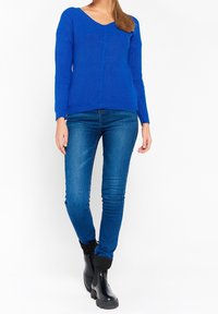 Blå stickad tröja med V-halsringning, med ribbat mönster och en central kabeldesign. Matchad med slim-fit blå jeans och svarta ankelstövlar.