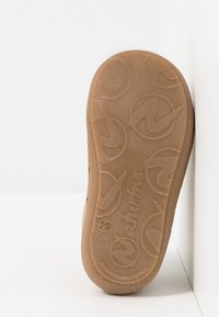Braune Gummisohle mit kreisförmigem Branding-Muster und strukturiertem Oberflächen. Enthält ein erhabenes Logo und die Größe "20" geprägt.