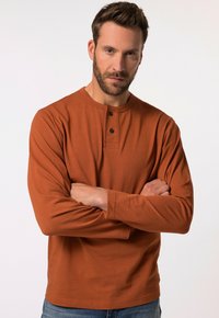 Långärmad, rostfärgad skjorta med henley-krage, två knappar och en mjuk textur, i kombination med blå denimjeans.