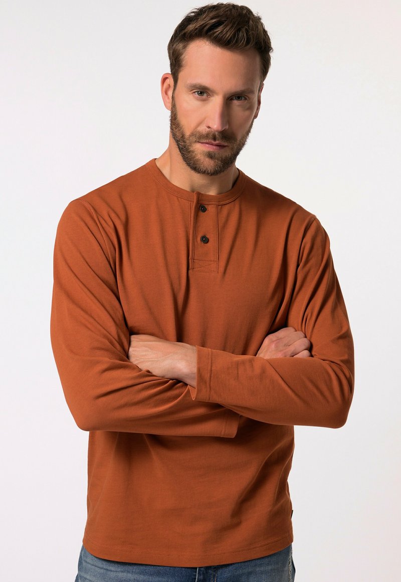 Långärmad, rostfärgad skjorta med henley-krage, två knappar och en mjuk textur, i kombination med blå denimjeans.