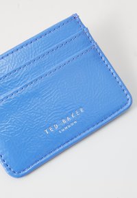 Modrý vegan koženkový obal na karty s textúrovaným povrchom, štyrmi slotmi na karty a kovovým logom "TED BAKER LONDON" v spodnom rohu.
