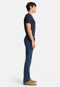 Jeans fitted blu scuro, in misto cotone, gamba dritta, cinque tasche, abbinati a una t-shirt nera a maniche corte e stivali in camoscio color sabbia.