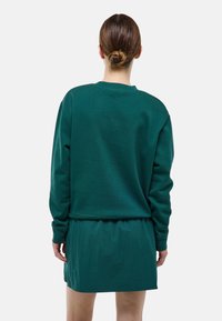 Sweat-shirt vert à manches longues, col rond et coupe décontractée, associé à une jupe verte assortie. Texture lisse, design minimaliste.