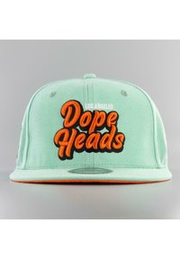 Vaaleanvihreä baseball-lippalakki, jossa on oranssi kirjailtu "Dope Heads" -logo ja "LOS ANGELES" -teksti yläpuolella, litteällä lierillä ja ommelluilla yksityiskohdilla.