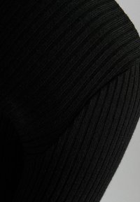 Schwarzer Rippstoff mit einer strukturierten Oberfläche; verfügt über glatte, konturierte Nähte und ein figurbetontes Design, das die Dehnbarkeit des Materials betont.