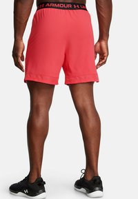 Raudoni sportiniai šortai su juodu elastiniu juosmeniu, ant kurio yra "Under Armour" logo. Norint užtikrinti vėdinimą, apačioje yra tinkliniai akcentai.