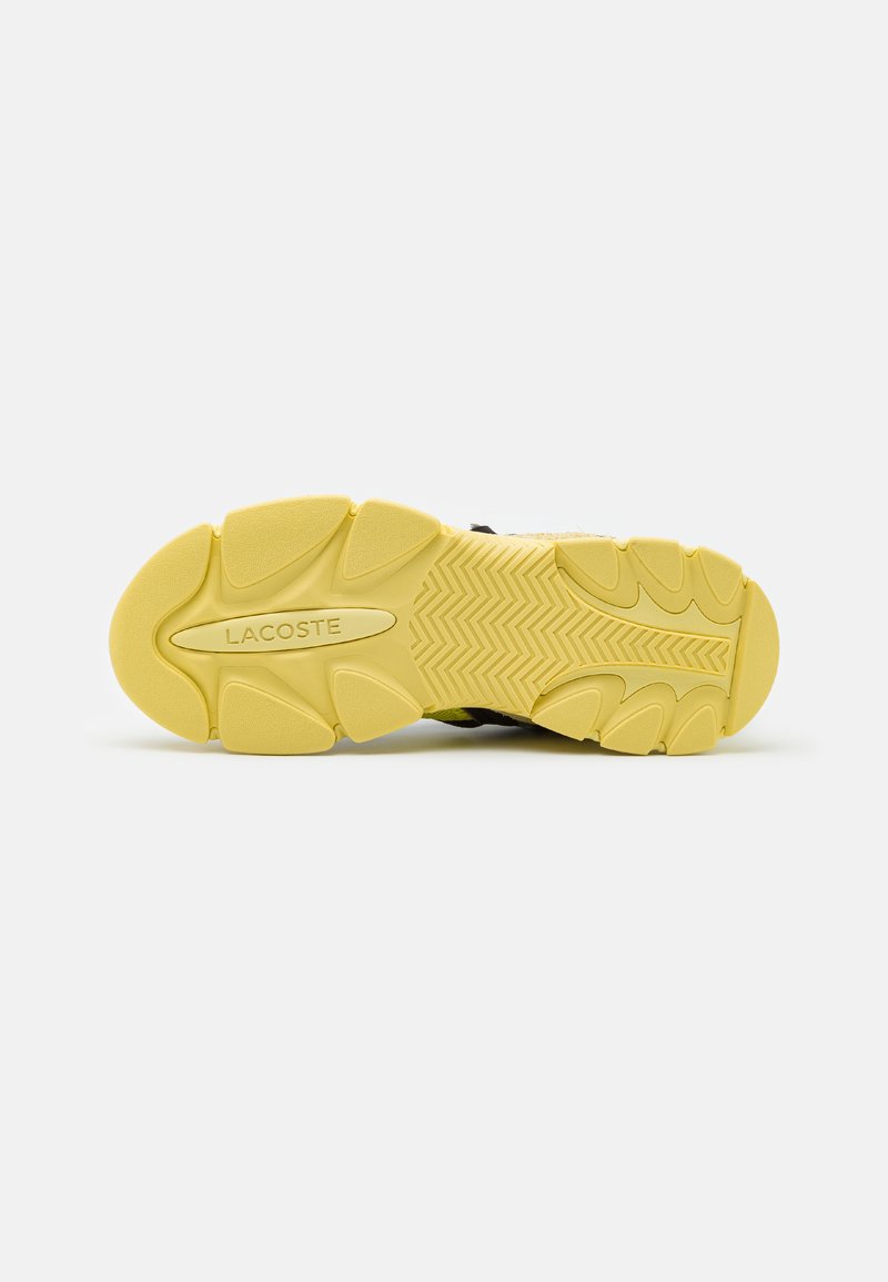 Suela de zapatilla Lacoste con una construcción de goma amarilla, superficie texturizada y un prominente patrón de zigzag en la banda de rodadura, con etiqueta de marca.