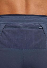 Granatowe szorty sportowe wykonane z aktywnego materiału, wyposażone w tylną kieszeń na zamek, teksturowany pas i gładką tkaninę, zaprojektowane z myślą o komforcie i funkcjonalności.