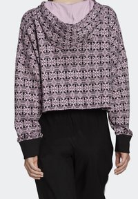 Mikina ve stylu háčkování v světle růžové barvě s černými geometrickými vzory, zkrácený střih, dlouhé rukávy a černé žebrované manžety.