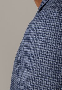 Niebieska koszula w wzory wykonana z teksturowanej tkaniny. Posiada kołnierzyk oraz kieszeń na piersi po lewej stronie dla dodatkowego detalu.