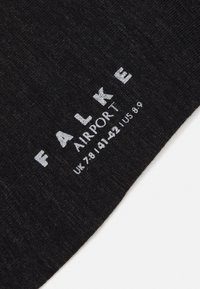 Crna čarapa izrađena od teksturirane tkanine, s natpisom "FALKE AIRPORT" i detaljima veličine otisnutim u bijelom, prikazuje jednostavan dizajn.