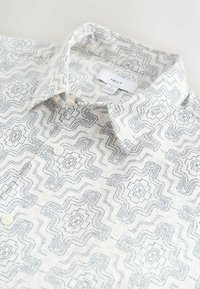 Kortærmet skjorte i let materiale med hvid baggrund og blåt geometrisk mønster, der har en spids krave og knaplukning.