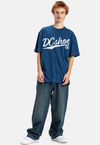 Navyblå bomull T-shirt med vit "DCshoe Co"-logotyp, kombinerad med löst sittande mörk denimjeans och vita sneakers. Avspänt, avslappnat passform.