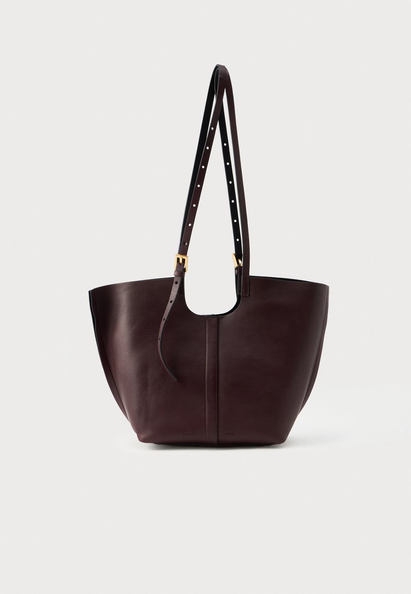 Bordeaux læder tote taske med en buet top og justerbar sort rem med guldfarvet hardware. Glat tekstur; minimalistisk design.