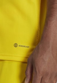 Geel sportshirt met een gestructureerd ontwerp, ademende stof en het "AEROREADY"-logo in de linkerbenedenhoek.