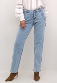 Jeans in denim azzurro chiaro con design a gamba dritta, cuciture visibili e tasche frontali. Abbinati a scarpe con tacco alto marroni.