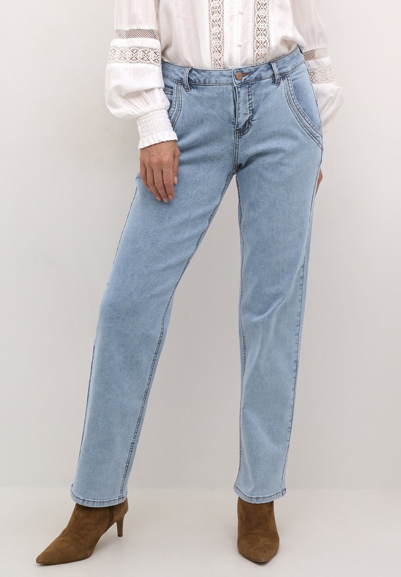 Jeans in denim azzurro chiaro con design a gamba dritta, cuciture visibili e tasche frontali. Abbinati a scarpe con tacco alto marroni.