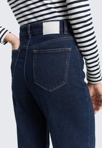 Ciemnoniebieskie dżinsy denimowe z tylną kieszenią ozdobioną jasną skórzaną łatą na pasku. Góra ma czarno-białe paski.