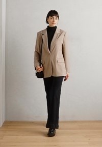 Blazer beige oversize avec revers, assorti à un col roulé noir et à un pantalon flare en denim foncé. Chaussures noires et petit sac inclus.