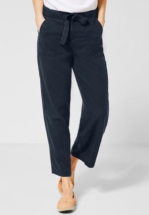 Femme portant un pantalon large noir avec poches avant et taille nouée, associé à des espadrilles plates couleur beige.