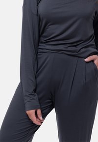 Maglia grigia scura a maniche lunghe con design arricciato in vita, abbinata a pantaloni a vita alta coordinati con pieghe sottili e tasche laterali.
